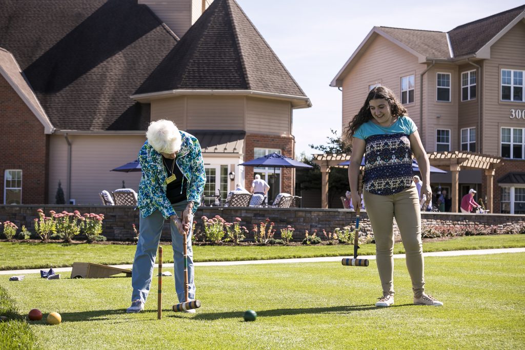Senior lady and study playing croquet in front of apartment buildings