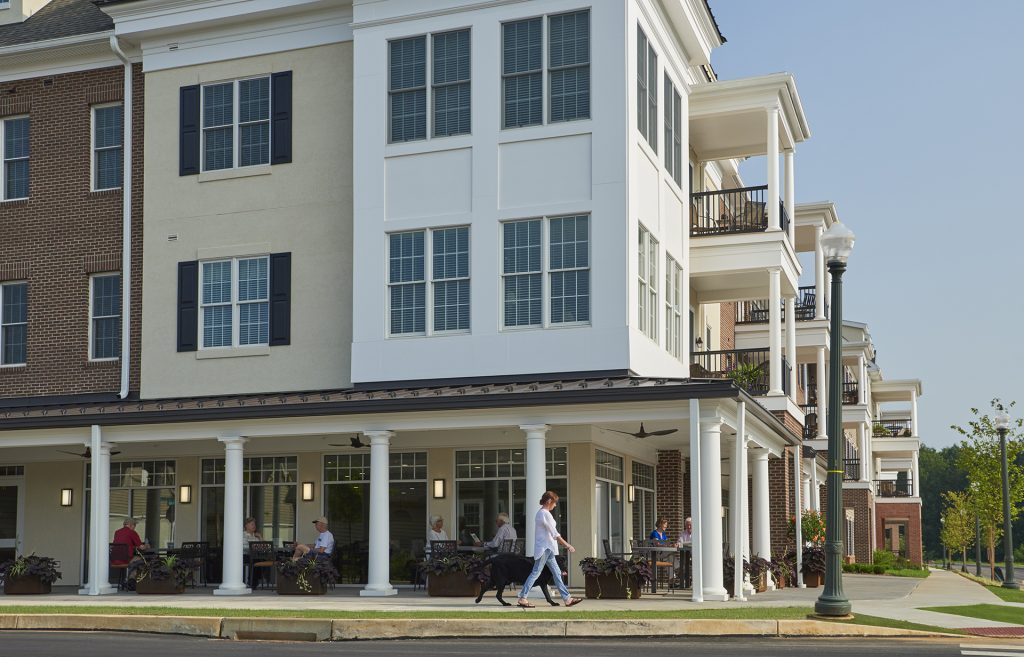 Woman walking dog in front of outdoor tables at apartment building