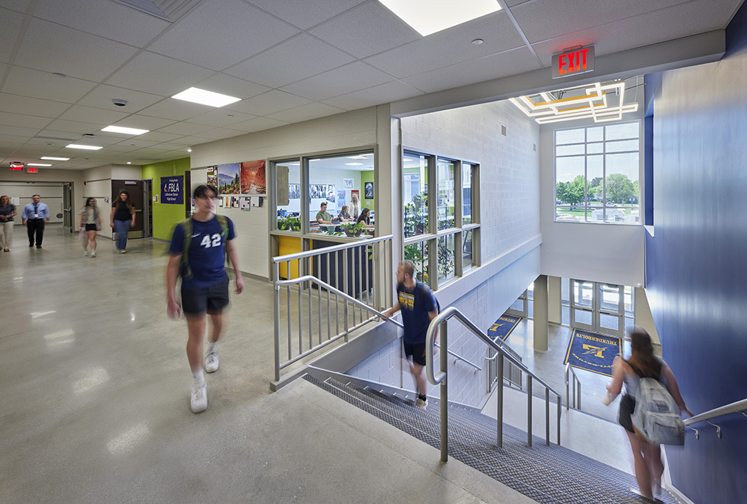 Students walking in a bright daylit hall and stairway of a school