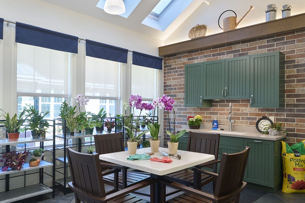greenhouse space with brick wall, table with plants, green cabinets, and windows