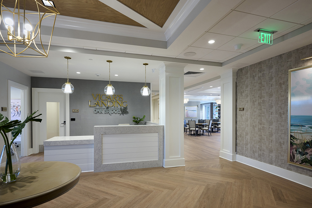 Assisted Living lobby space with reception desk, herringbone wood floor, and logo signage