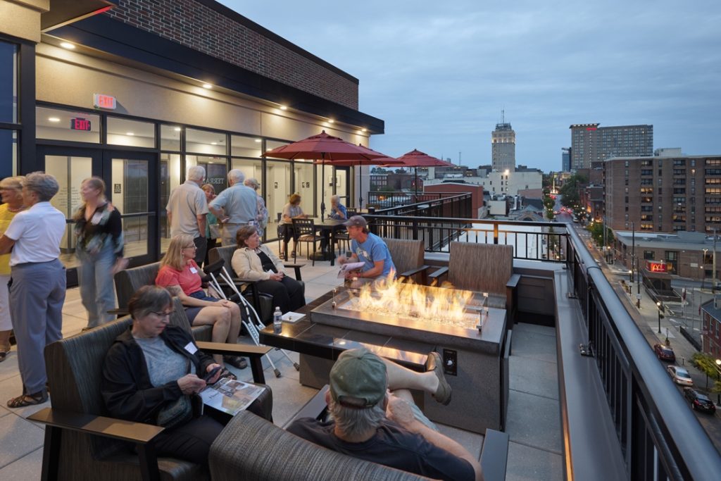 Rooftop balcony with people sitting by firepit with city views