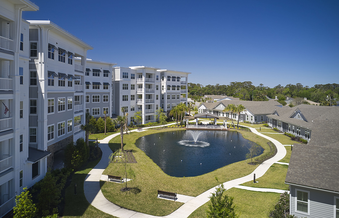 Multi-story hybrid apartment building with adjacent pond and cottages