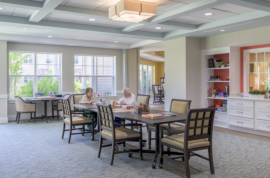 Memory support activity room with movable tables, abundant natural light, and built-in storage for games, puzzles, and creative activities.