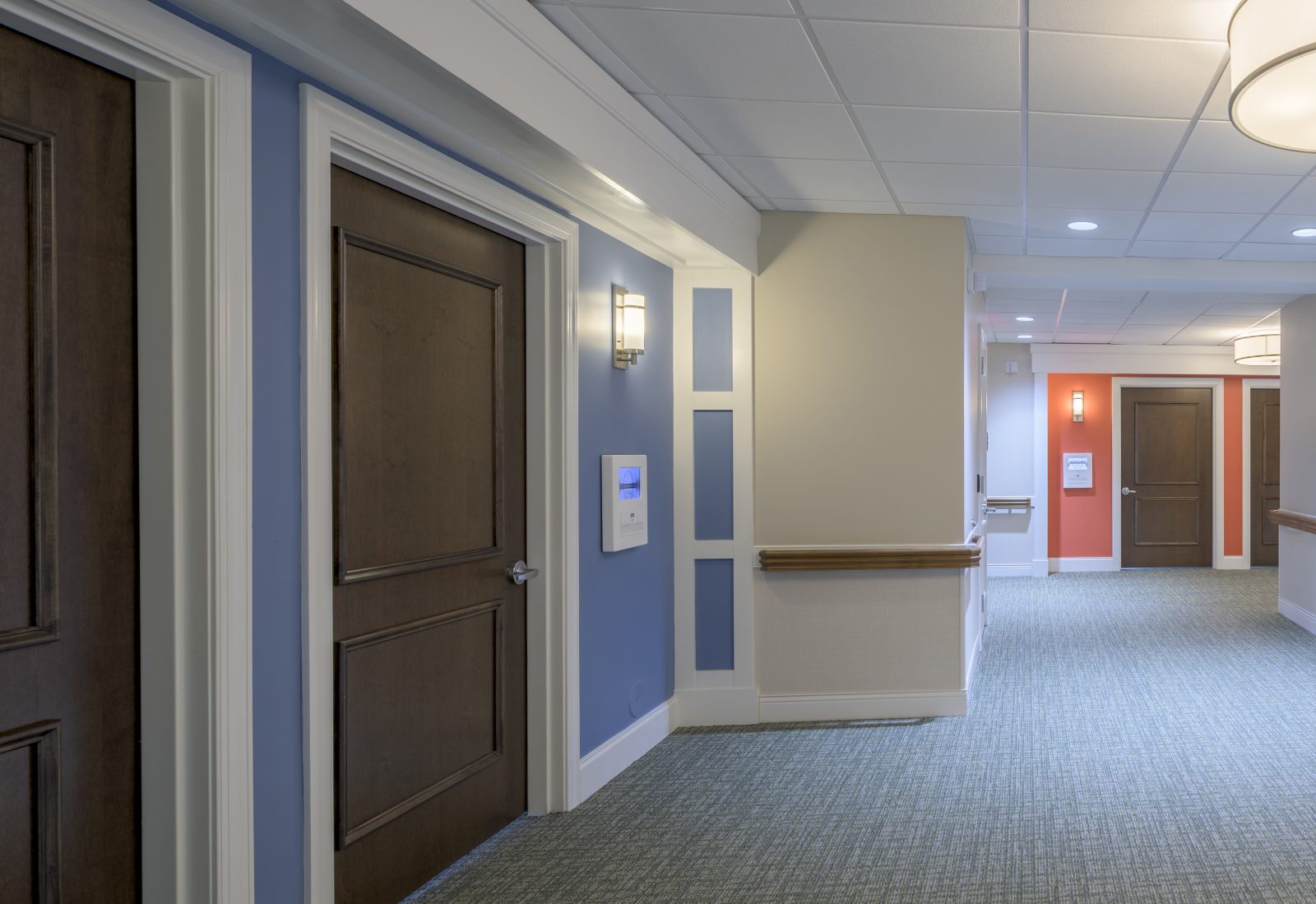Corridor for memory care residences with different color accents outside doorways to help with wayfinding