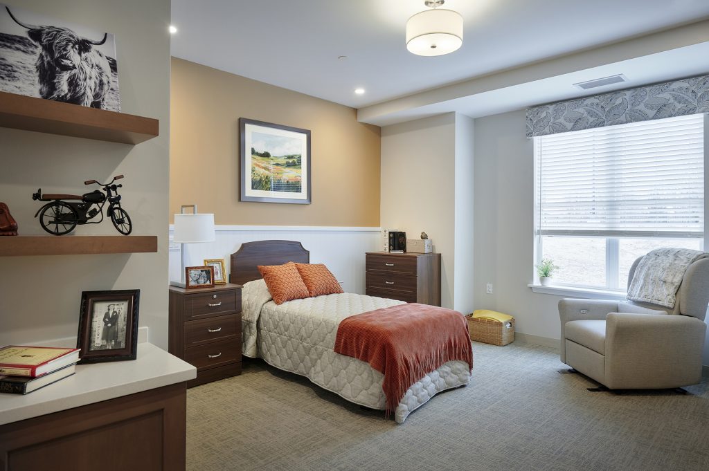 Resident room in memory care neighborhood with large window and shelving with personal items