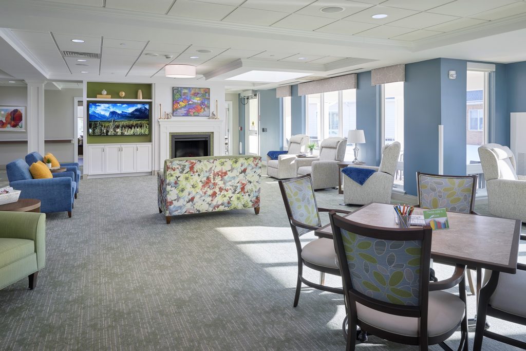 Memory care neighborhood living room with lots of windows, bright colors and a fireplace