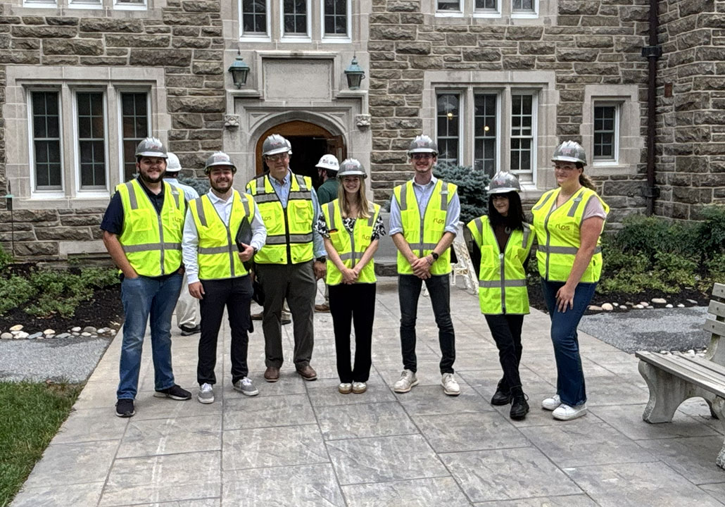 Group of people in hard hats and construction vests in front of academic building under renovation
