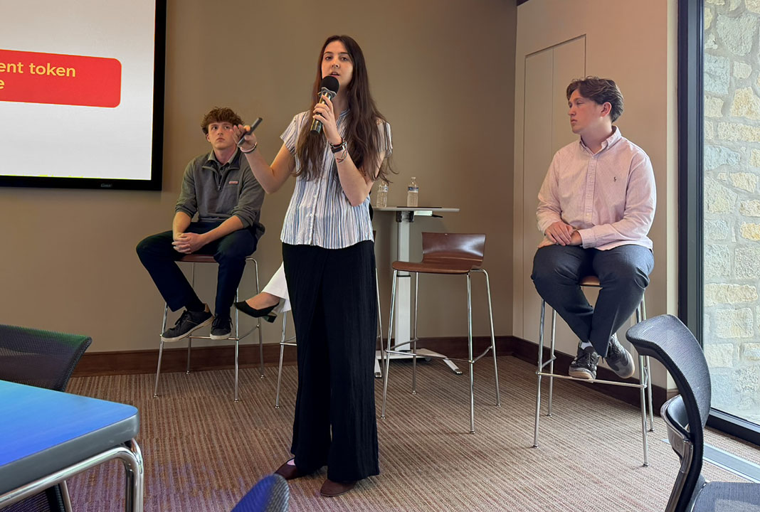 Woman talking into a microphone with three individuals sitting behind her